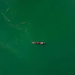 A minimalist top-down view of two boats on the emerald green waters of Naukuchiatal. The simplicity of the composition highlights the peacefulness of the lake and the subtle textures on the water's surface.
