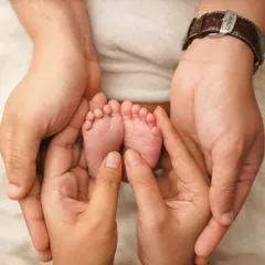 Both parents' hands come together to create a protective cup around their newborn's feet. This shot beautifully represents the love and security surrounding the new baby.