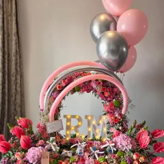 A modern and celebratory arrangement featuring a floral wreath, light-up initials, and balloons. This personalized hamper is perfect for birthdays and milestone celebrations.