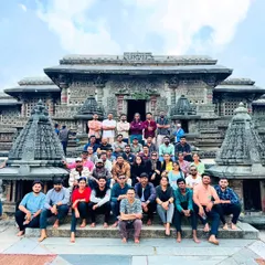 A large group seated on the steps of a beautifully carved Hoysala temple. These sites provide a stunning backdrop for group photos and a deep dive into Karnataka's history.