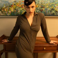 A confident and powerful pose against a clean, architectural background. The lighting highlights the model's form and the texture of the dress.