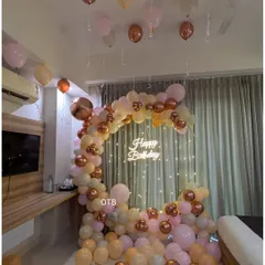 A cozy and elegant room setup featuring a circular balloon arch with a neon sign and fairy lights. The pastel and rose gold balloons create a warm and inviting atmosphere.