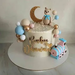 A cute first birthday cake for "Baby Dhruv." This no-fondant design features a teddy bear, a crescent moon, and a little train in soft pastel colours.