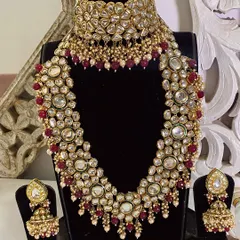 A full display of a classic bridal kundan set with ruby bead detailing. This includes a choker, a layered necklace, and matching jhumka earrings, available for rent or purchase.