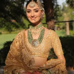 A happy bride glowing in her golden ensemble. The styling focuses on the stunning contrast between the gold outfit and the vibrant green of the heritage jewelry.