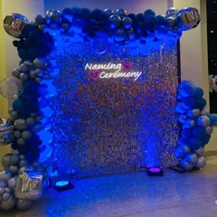 The same naming ceremony setup under deep blue lighting. This shows how versatile a sequin wall can be for creating different moods throughout an event.