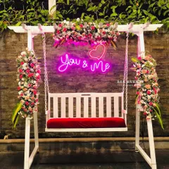 A full view of the elegant floral swing with its "You & Me" neon sign. This has become one of our most requested photo booth setups, blending modern romance with beautiful floral design.