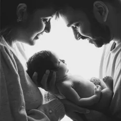 A high-key black and white portrait that feels light, airy, and full of hope. The focus is entirely on the connection between these new parents and their baby.