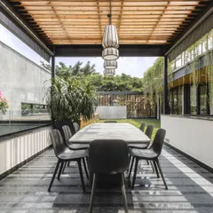 This outdoor covered dining deck is an inviting extension of the home, perfect for enjoying Bangalore's pleasant weather year-round. A wooden pergola provides partial shade.