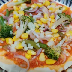 A pizza base topped with my homemade sauce and fresh vegetables like broccoli, corn, and onions, ready for the oven.