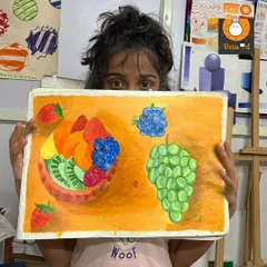 A proud student displays her vibrant fruit painting. This piece demonstrates a great understanding of color, composition, and how to render different textures using acrylics.