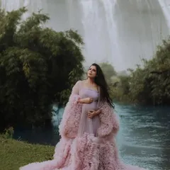 A serene monsoon maternity shoot. This client looks absolutely peaceful in a light pink ruffled gown with a matching sheer robe, set against a stunning waterfall. The soft fabric and design are perfect for capturing tranquil moments.