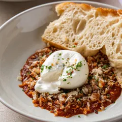 Burrata served over a savory tomato base with a slice of crusty bread. This image focuses on the creamy texture of the cheese and the rustic presentation.
