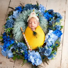 Even the tiniest newborns can join the celebration. This sleeping baby is swaddled in yellow and posed as little Krishna with a flute and peacock feathers in a floral nest.