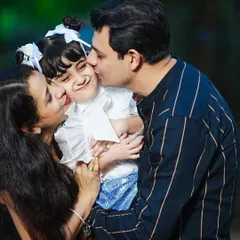 A heartwarming moment of family affection, with both parents kissing their daughter's cheeks during a sunny outdoor session.