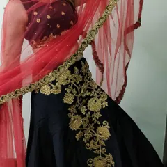 A detailed shot of the black lehenga, focusing on the heavy gold floral embroidery that climbs up the side of the skirt. The contrasting red dupatta adds a pop of color.