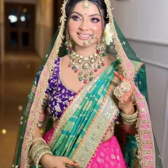 A beautiful bride in a multi-colored lehenga with a green dupatta. The makeup features a soft pink blush and a nude lip to balance the vibrant outfit.