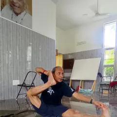 Practicing a variation of Eka Pada Sirsasana under the watchful eye of Guruji. This pose requires significant hip flexibility and core strength, developed through consistent and mindful practice.