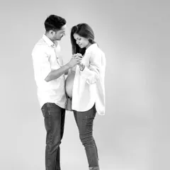 This black and white portrait captures a candid, gentle interaction between the expecting parents. Dressed in simple, coordinating outfits, their connection and the beautiful silhouette of the baby bump are the focus.