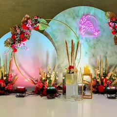 A modern photo-op corner featuring circular backdrops with a marble texture. The design is accented with a custom neon monogram, pampas grass, and red florals, blending contemporary and romantic elements.