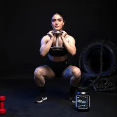 An action shot demonstrating a lifestyle application of the product. The female model is mid-squat, associating the supplement with strength and performance. The product is placed clearly in the foreground, ensuring it remains the focus even during a dynamic scene.