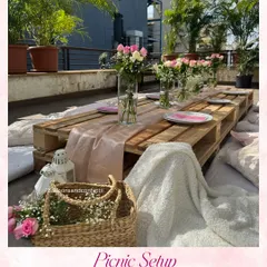 A perfect picnic setup for a sunny day. This features a low table made from wooden pallets, surrounded by comfy floor seating, and decorated with fresh pink and white roses.