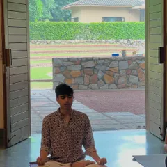 A young participant finds his center, meditating at the threshold of the yoga hall, with the green outdoors just beyond. These retreats offer a serene space for all ages to connect with their inner selves.