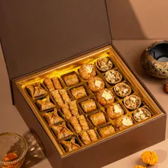 An elegant shot of an open box of assorted baklava and other Indian sweets from Mr Brown bakery. The warm lighting and festive props create a luxurious feel for this gift hamper.