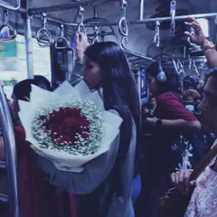 A different angle of the woman with roses on the train, showing more of the crowded compartment. Her personal moment of self-love or anticipation contrasts with the public commute.