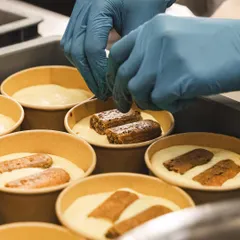 A chef carefully places coffee-soaked ladyfingers into the cups for our Tiramisu. Each layer is built with precision.
