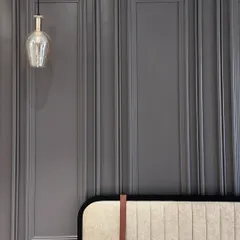 A detail shot of a custom headboard against a grey paneled wall. The design features a unique leather strap detail, adding a subtle, sophisticated touch.