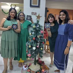 Friends gather around a Christmas tree, holding up the dot mandala art they created during a festive holiday party.