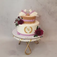 This elegant two-tier engagement cake features a hand-painted gold monogram, fondant love bird toppers, and a realistic wood-bark texture on the top tier. The design is tied together with deep red chrysanthemums and delicate purple ribbons.