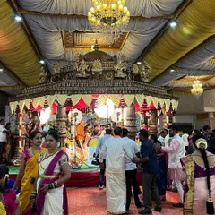 A wide view of a wedding hall featuring a grand, ornate Muhurtham mandap. The scale of the mandap makes it the undeniable centerpiece of the entire venue.