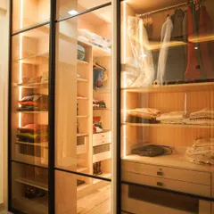 A glimpse into a custom walk-in closet, where luxury meets organization. This design features transparent glass doors, integrated LED lighting, and ample shelving to display and store your collection, turning your wardrobe into a personal boutique.