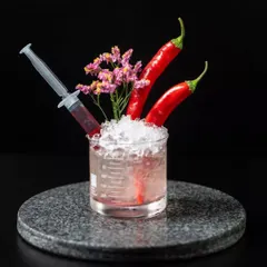 A spicy and scientific creation. This cocktail is served in a beaker with fresh chilies, a syringe of raspberry coulis, and crushed ice, allowing the guest to customize their level of spice and sweetness.
