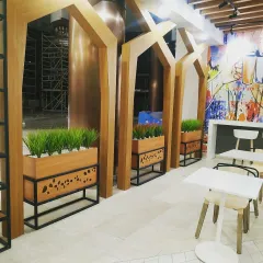 This wide shot shows how I used a series of custom planters to define the seating area in a cafe. The combination of wood, metal, and vibrant green artificial grass creates a modern and relaxing environment for customers.