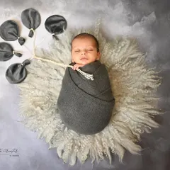 Floating away on a cloud of dreams. This creative shot features a swaddled newborn holding a bouquet of grey balloons, creating a whimsical and artistic portrait.