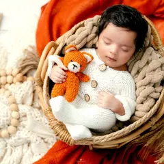 Warm, earthy tones create a cozy atmosphere for this newborn portrait. The baby, dressed in a knitted outfit, cuddles a teddy bear while nestled in a woven basket.
