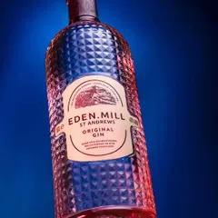 An experimental shot of an Eden Mill Gin bottle, playing with dramatic angles and colored lighting. The red and blue lights create a vibrant, energetic feel and highlight the intricate texture of the glass bottle.
