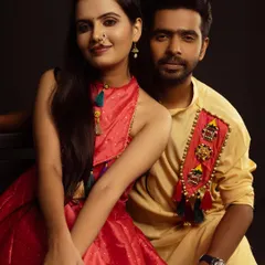 A charming studio portrait of a couple in coordinated fusion wear. They are seated close together, looking at the camera with warm smiles.