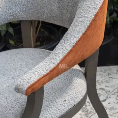 A close-up on the craftsmanship of the Versa Armchair. This detail shows the contrast between the soft bouclé, the corded orange accent, and the deep earthy brown finish of the solid ash wood frame.