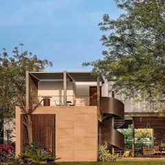 An alternate view of the Abhikram residence, showing the interplay between the solid brick structure, the open patio, and the sculptural form of the external staircase.