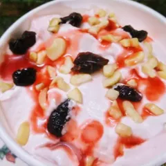 A creamy and delicious plant-based dessert, possibly a vegan shrikhand, topped with nuts, raisins, and a sweet syrup.