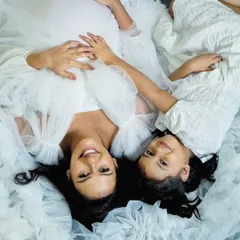 An artistic top-down shot showing the beautiful connection between a mother and daughter. The flowing white fabric creates a soft, dreamy atmosphere for this maternity portrait.