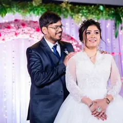 A sweet moment on the reception stage, with the groom's hands on the bride's shoulders, both looking out at their guests.