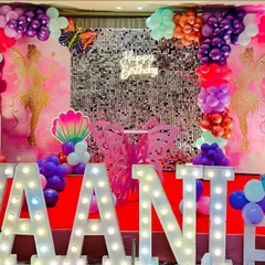 A vibrant fairy and butterfly theme for a child's birthday. This decoration features large pink butterfly wings, a silver shimmer wall with a neon "Happy Birthday" sign, and marquee letters spelling out the name "VAANI".