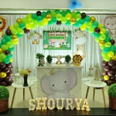 A fun and friendly jungle safari theme for a first birthday. This decoration includes a vibrant green and gold balloon arch, cute animal cutouts like a giraffe and lion, and a custom-designed dessert table featuring a baby elephant.