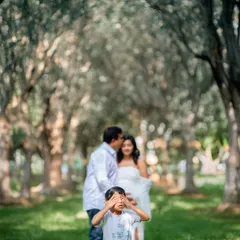 A playful family photo! The soon-to-be big brother covers his eyes while his parents share a kiss in the background. It's a fun way to capture the family's personality.