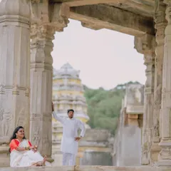 A wide shot of a couple posing amidst the stone pillars of a historic temple, with the gopuram visible in the background. This composition emphasizes the grandeur of the location.